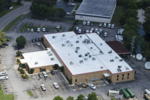 aerial view of white flat commercial building with parking lot filled with cars surrounding