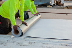 two maxwell roofings on their knees unrolling a large metal sheet on a commercial roofing project