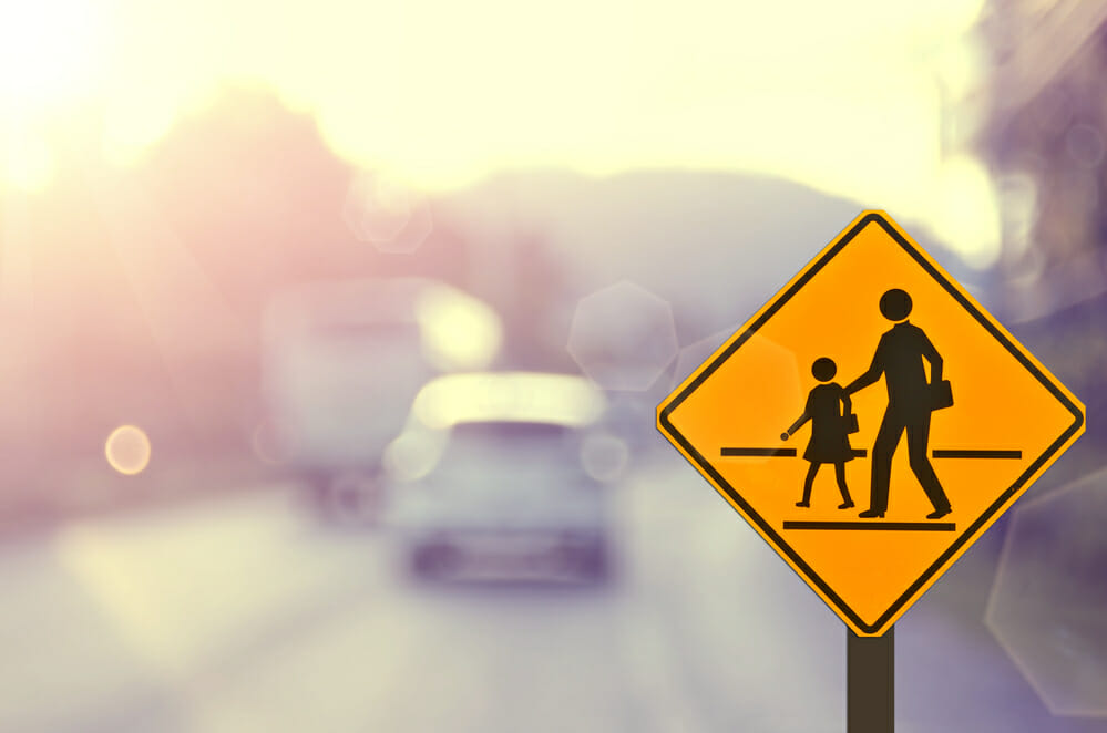 diamond-shaped yellow crosswalk in focus with blurred street and cars in the background