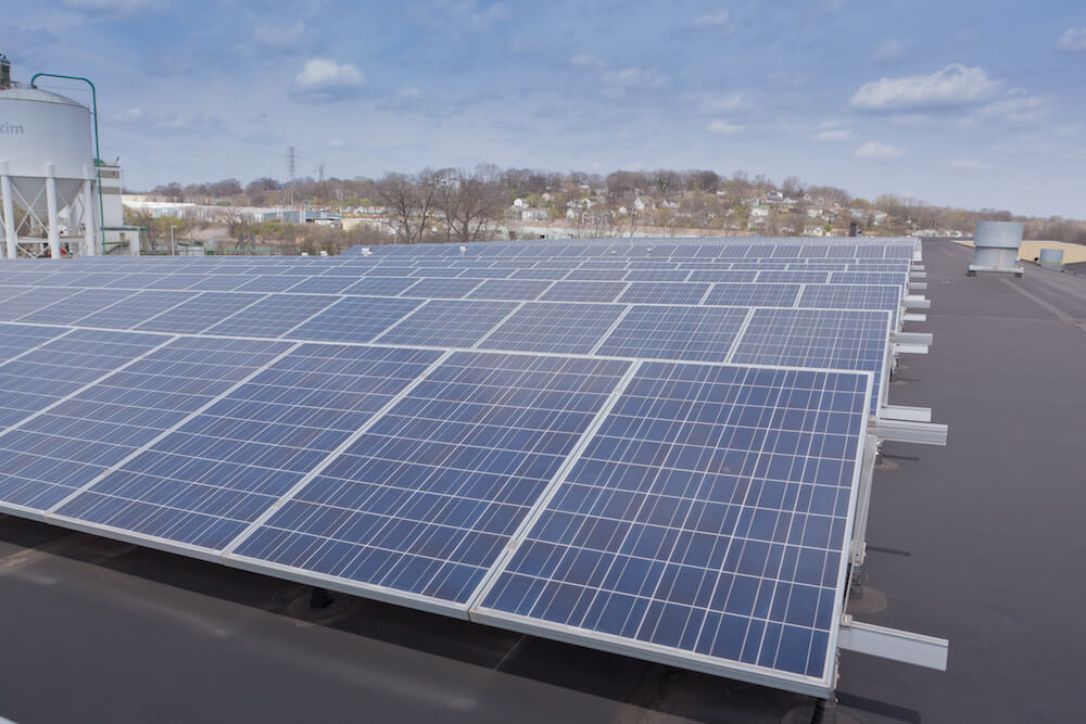 rows of solar panels on rooftop of a commercial building with water tower in the background