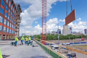 workers at construction site with a red crane lifting roof materials