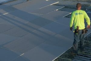 Maxwell worker with neon yellow shirt walking across unfinished roofing project as sun sets behind him