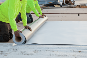 two maxwell roofers unrolling a large metal sheet on a commercial roofing project