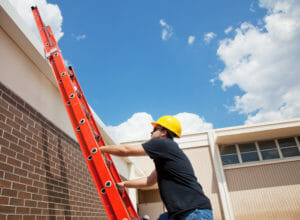 Worker climbing up a red ladder to the roof commercial building