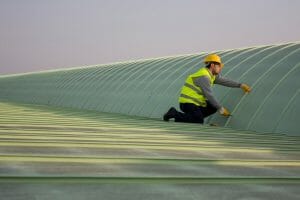 worker in neon yellow safety vest and yellow construction helmet working on metal commercial roof