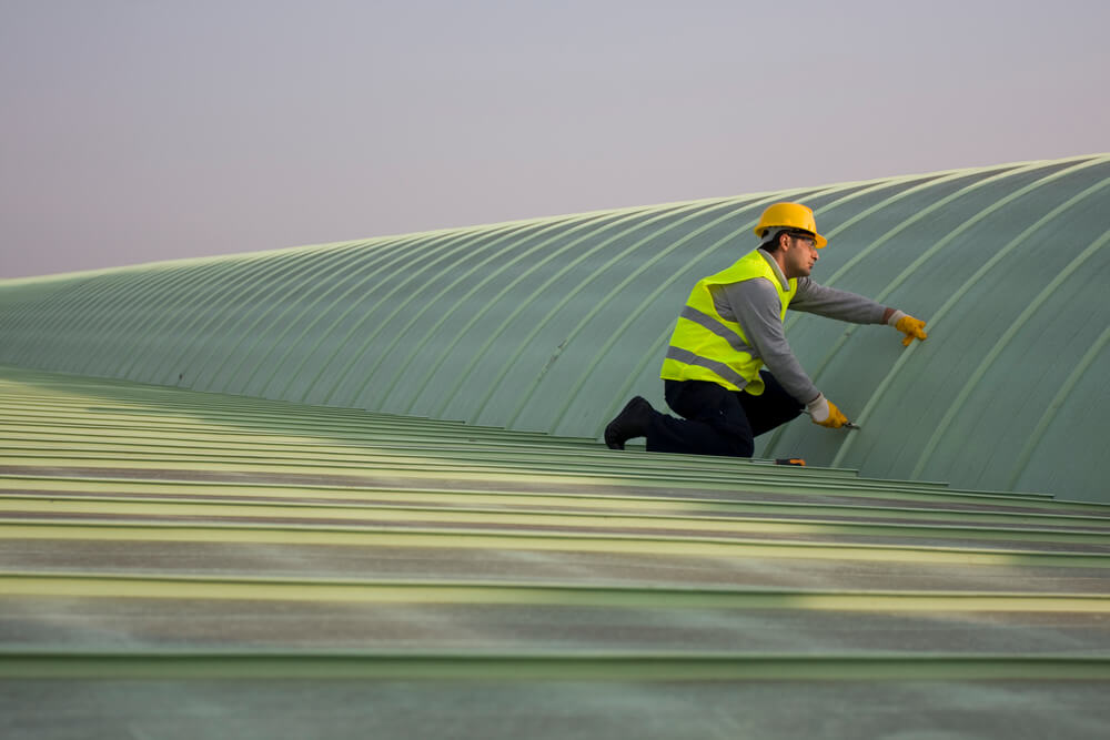 worker in neon yellow safety vest and yellow construction helmet working on metal commercial roof