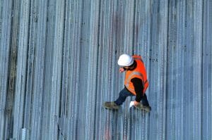 aerial view of worker in an orange safety vest and white helmet walking across metal commercial roof