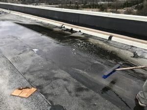 worker mopping debris from commercial roof with a broom