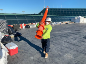 maxwell roofing specialist on commercial roof carrying a large stack of orange caution cones