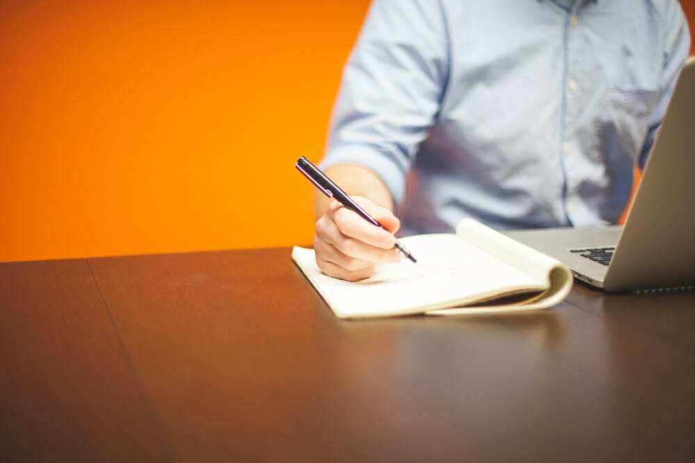 business man writing on notebook and working on laptop at table.