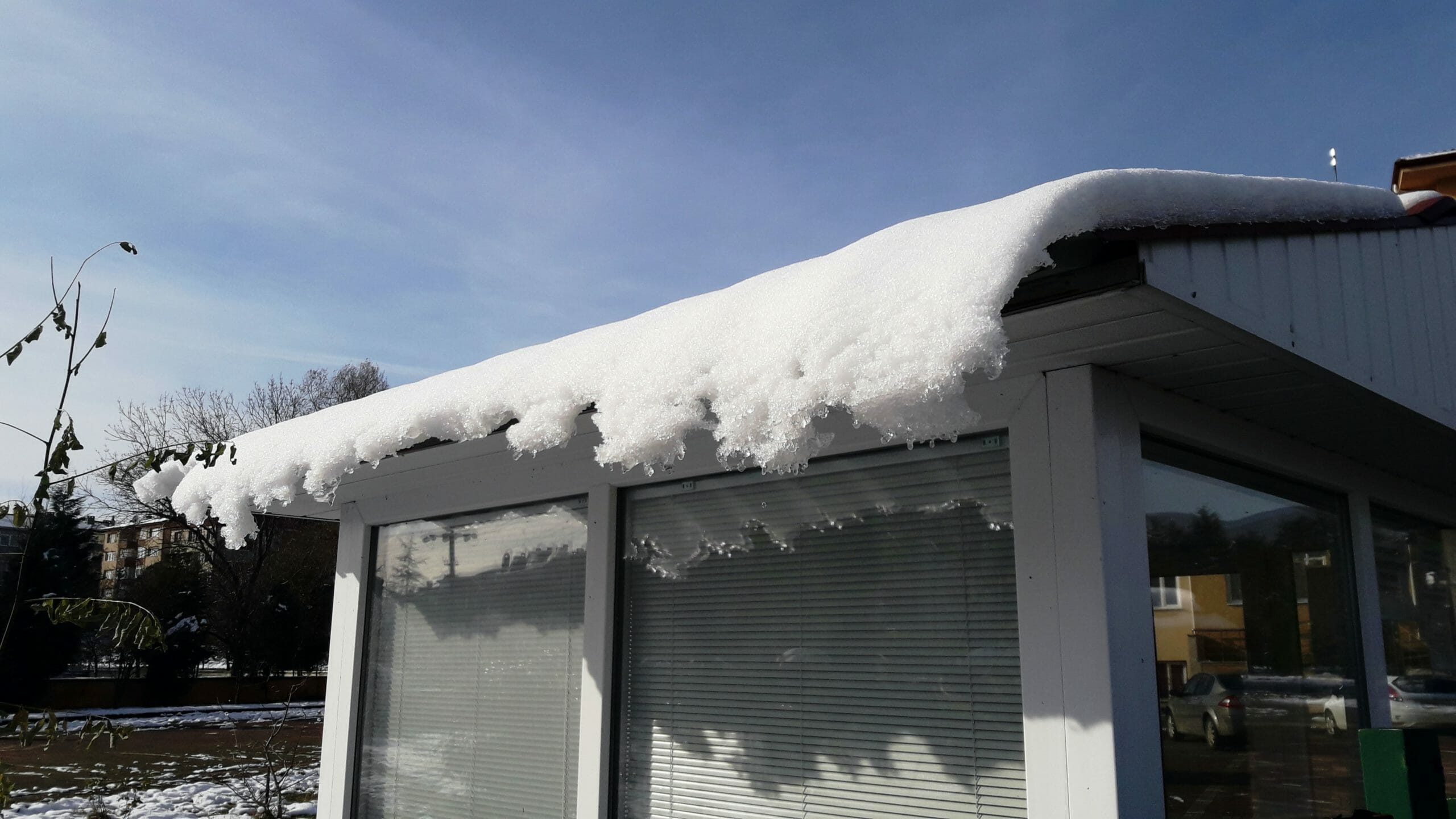 Commercial roof with snow and icicles hanging down over a window in the wintertime.