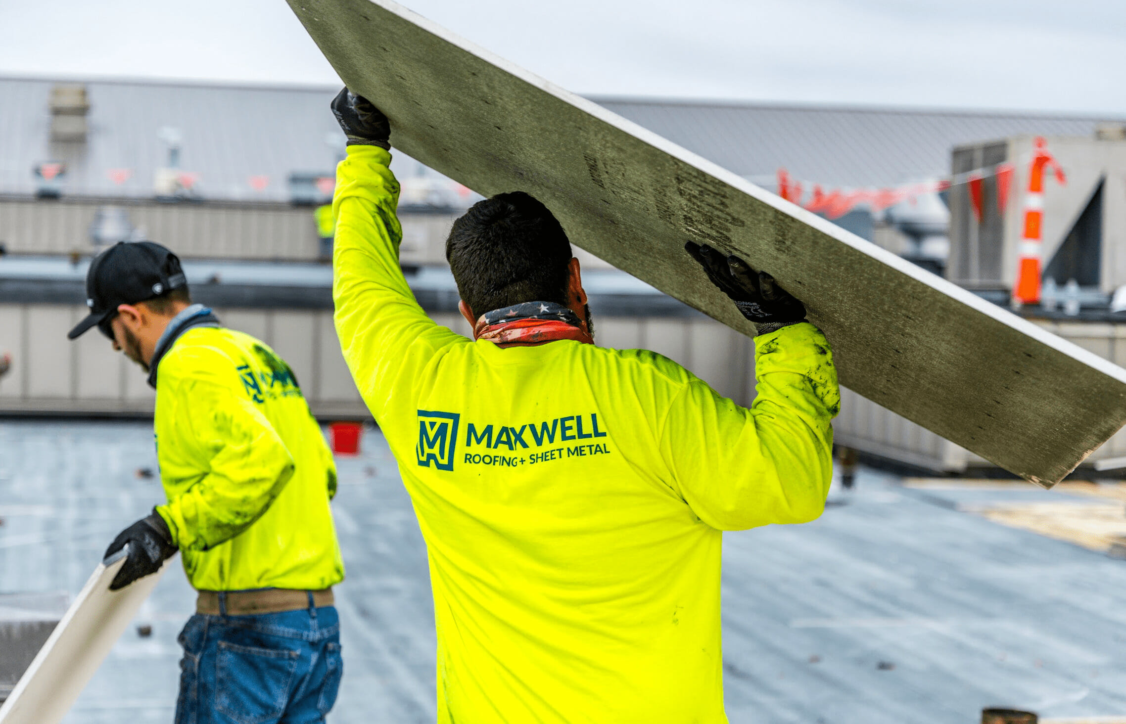 Maxwell Roofing Contractor in neon yellow logo shirt holding a board above his head.