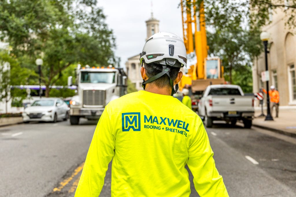 The back of a maxwell roofing worker walking down a busy city street