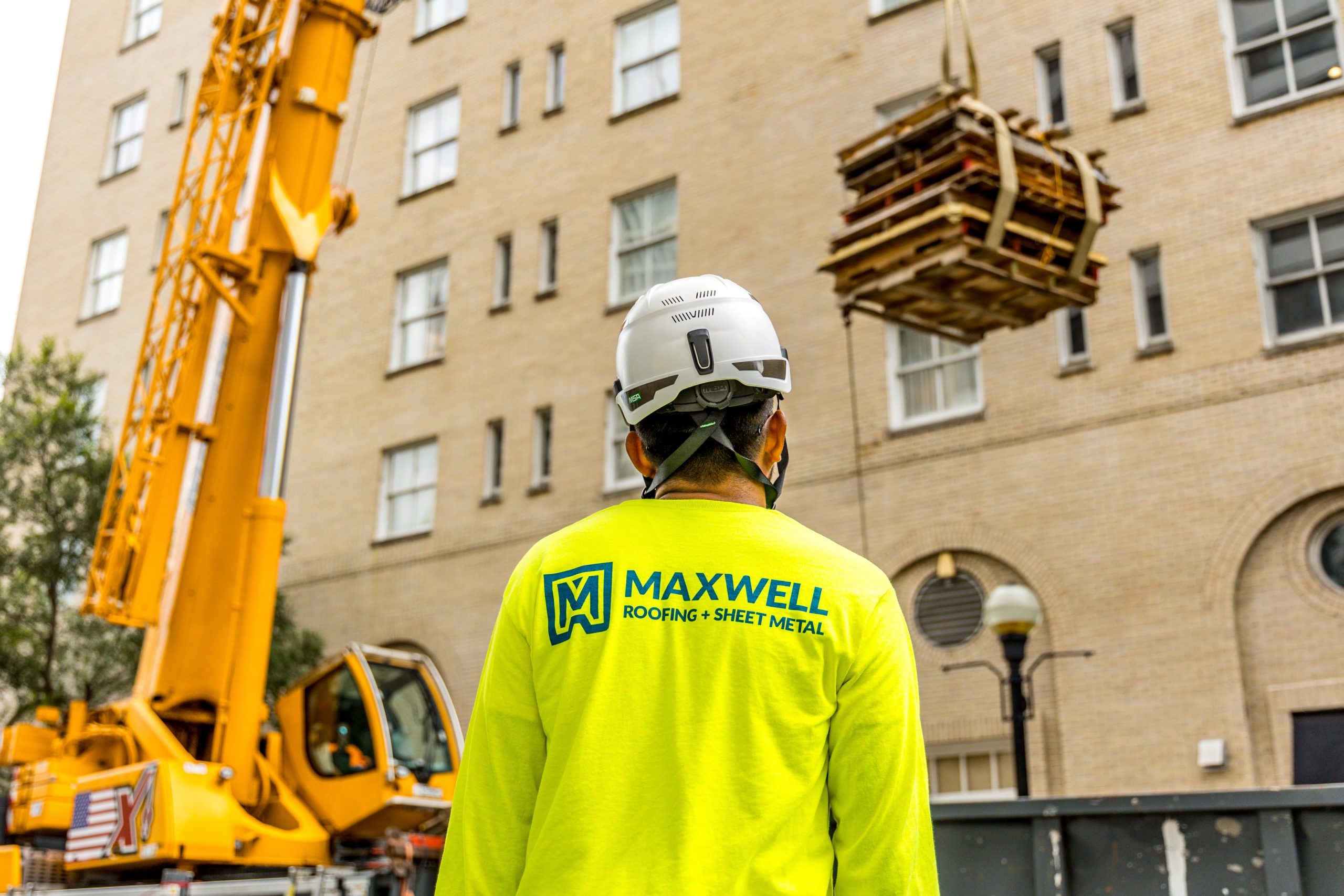 roofer in a hardhat looking up at a crane.