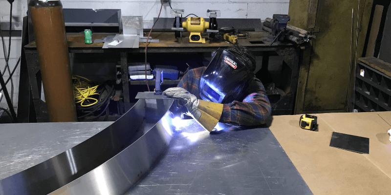 worker fabricating roofing materials with protective eye shield.